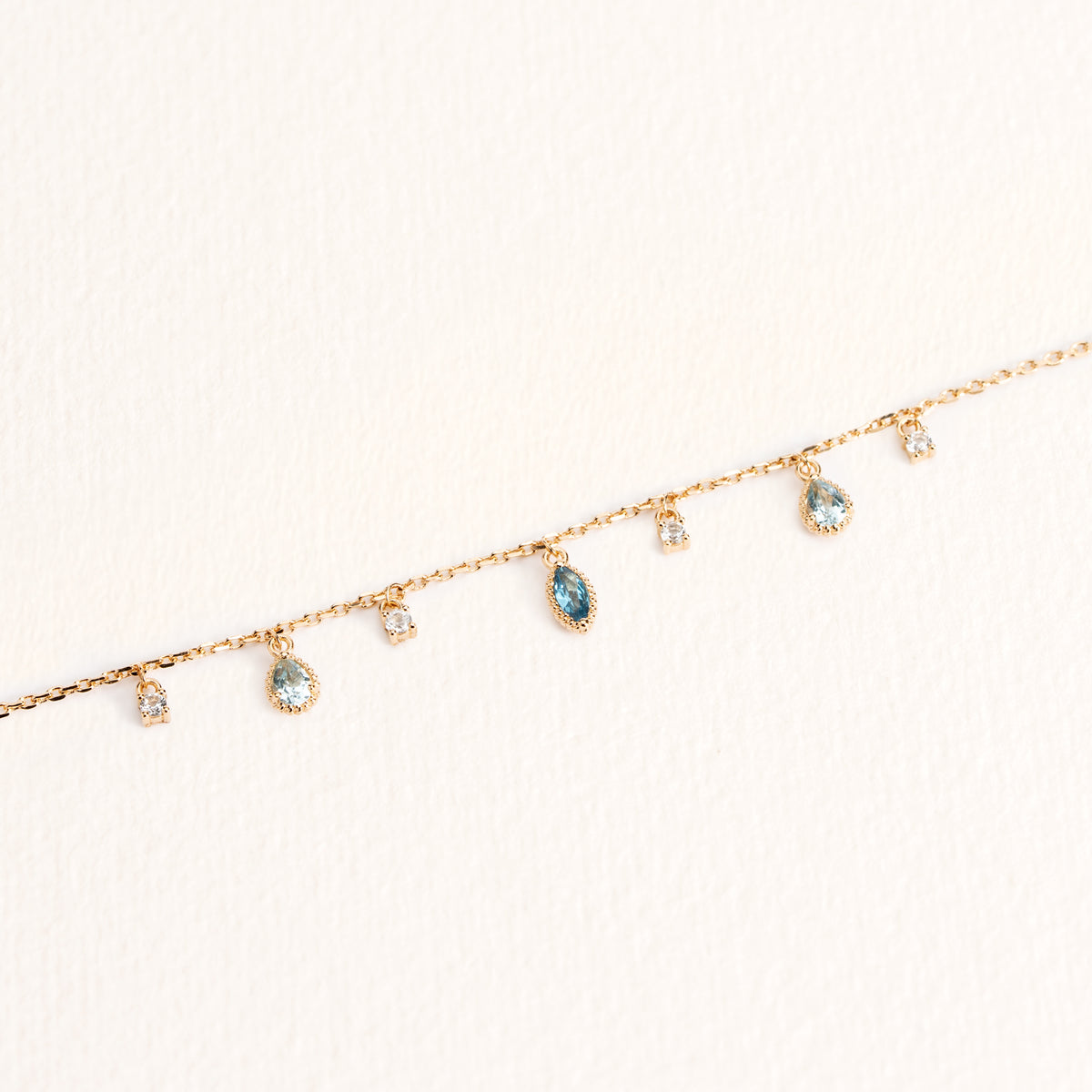 Bracelet Mira doré en plaqué or 18 carats avec chaîne fine ornée de topazes bleu profond, bleu clair et blanches